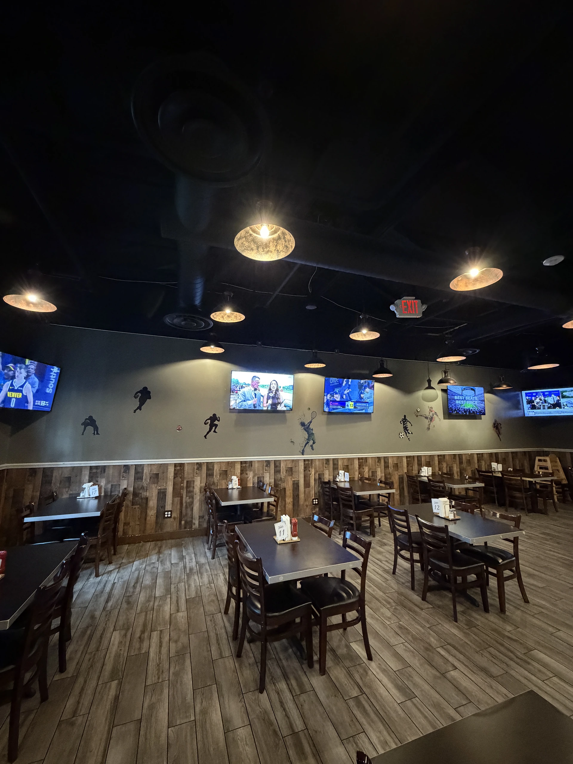 VJ’s dining room with warm pendant lights, tables, and live sports screens