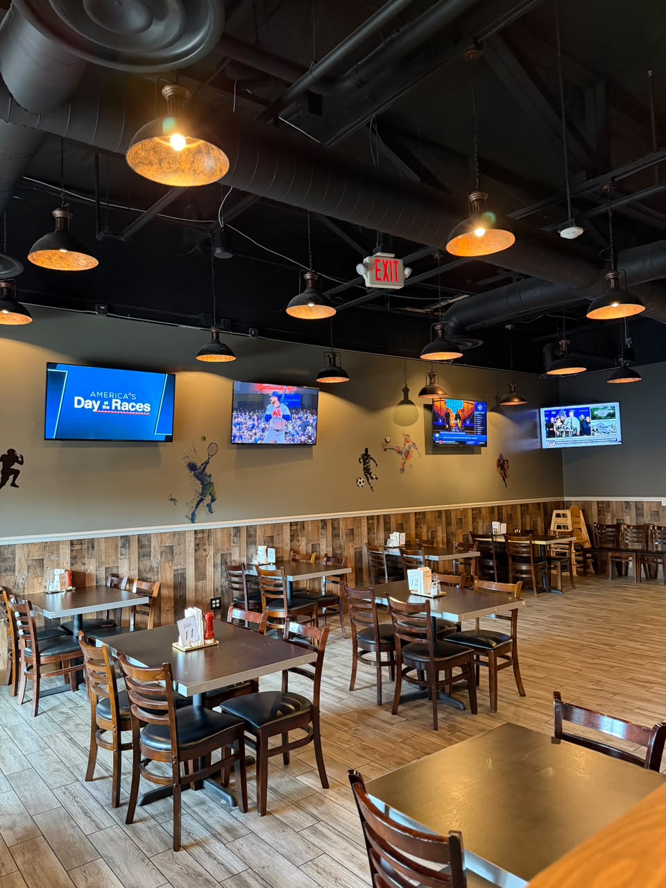 VJ’s dining area with wall-mounted sports TVs, warm pendant lights, and tables for watching the game